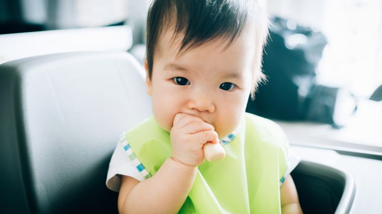Adorable baby eating baby finger biscuit on high chair